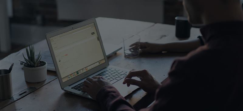 Person arbeitet konzentriert am Laptop an einem Holztisch