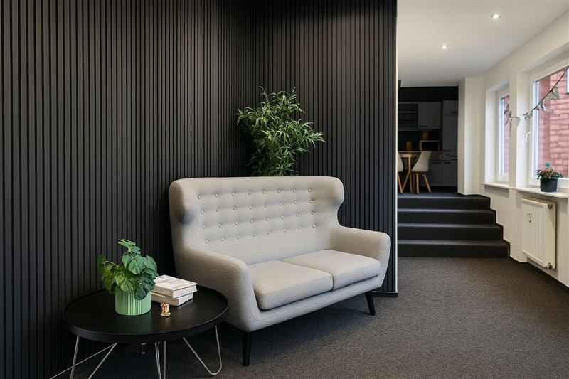 Lounge-Ecke mit grauem Sofa vor dunkler Lamellenwand und Grünpflanzen