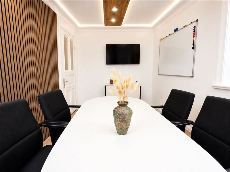 Meetingraum mit weißem Tisch, Bildschirm und Whiteboard