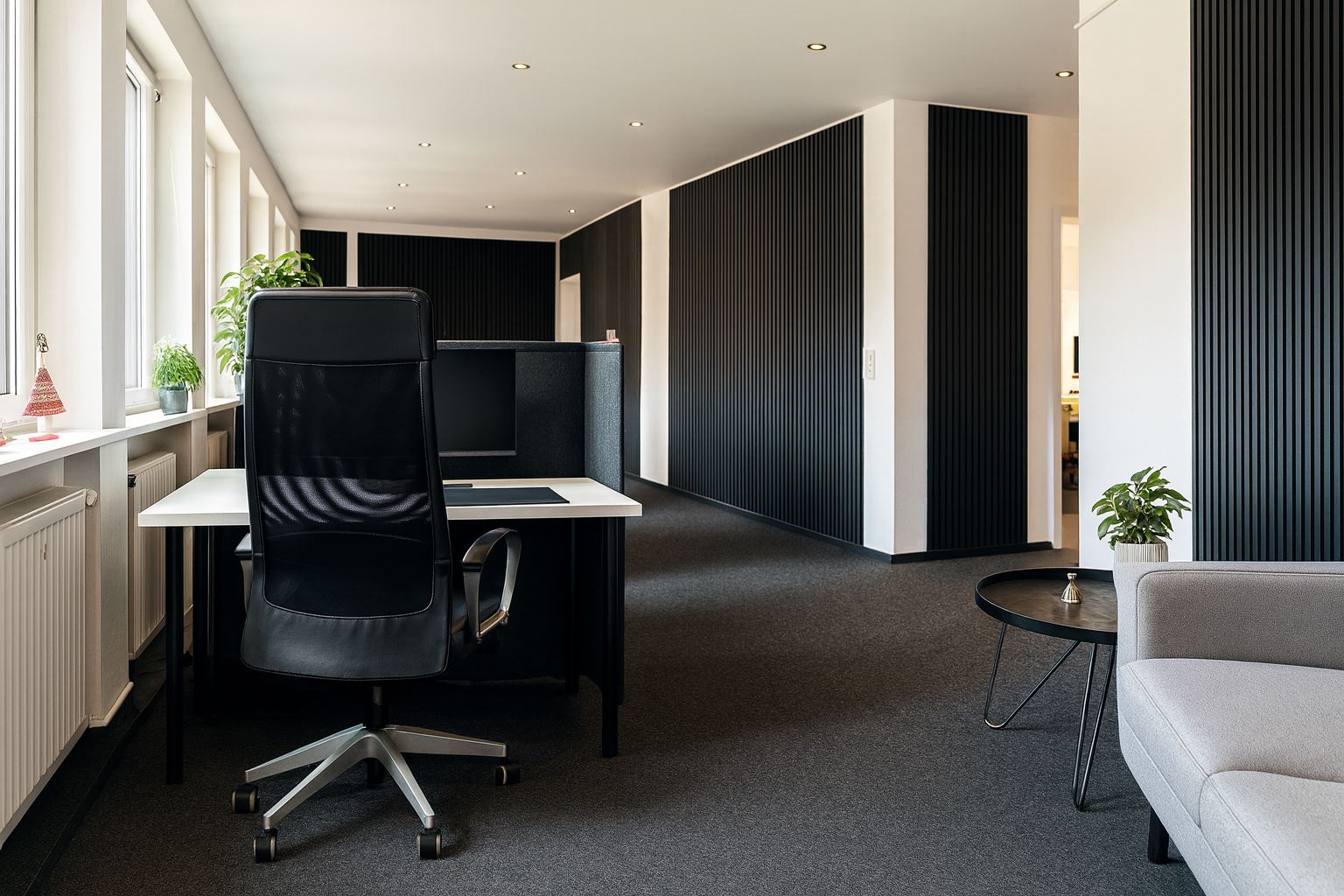 Heller Open Space mit Schreibtisch am Fenster, dunklen Lamellenwänden und Sitzecke